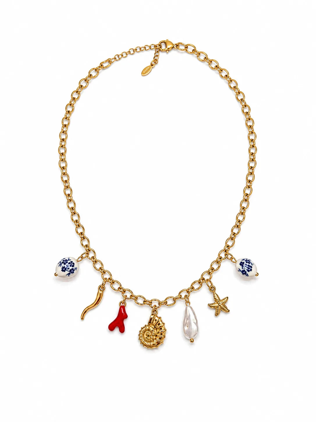 Collier Riviera à plat sur fond blanc studio, chaîne forçat d'or et 7 pendentifs visibles — perles de faïence bleu Moustiers, cornicello d'or, brin de corail rouge, médaillon soleil, perle baroque blanche et étoile ivoire