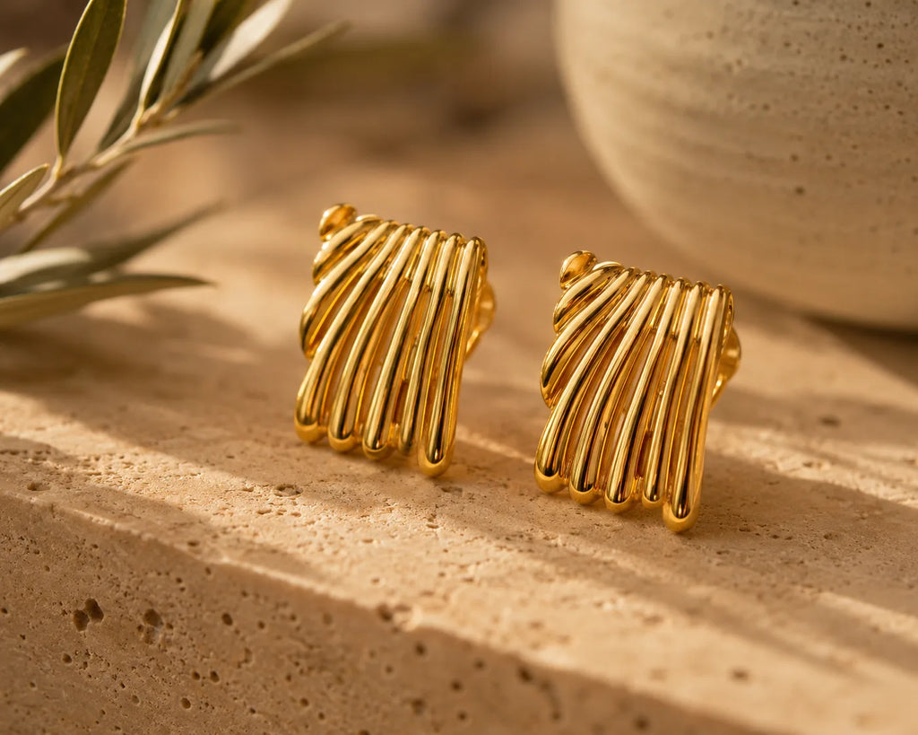 Boucles Duna posées sur un bloc de travertin crème, branche d'olivier à gauche et jarre artisanale en céramique en arrière-plan, lumière dorée