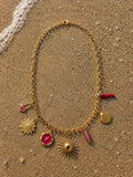 Collier Solina posé sur le sable doré humide d'une plage méditerranéenne, vague d'écume au coin haut-gauche, étiré en ovale, lumière dorée du couchant