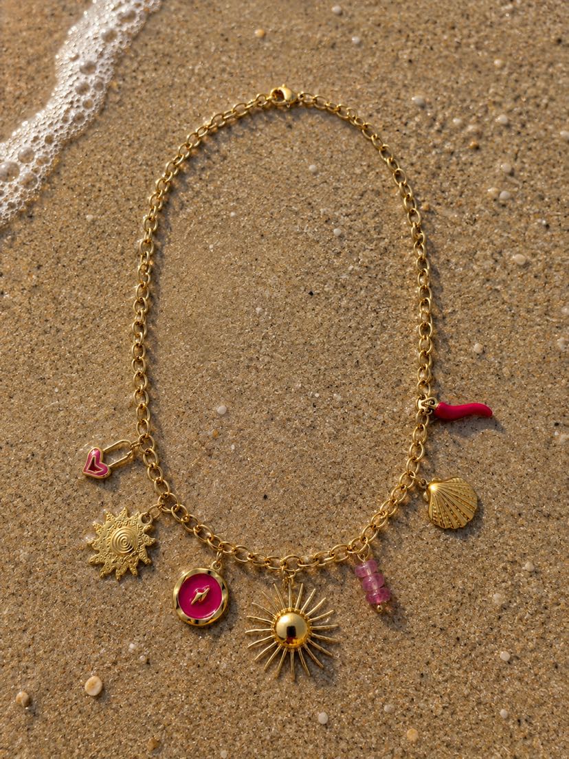 Collier Solina posé sur le sable doré humide d'une plage méditerranéenne, vague d'écume au coin haut-gauche, étiré en ovale, lumière dorée du couchant