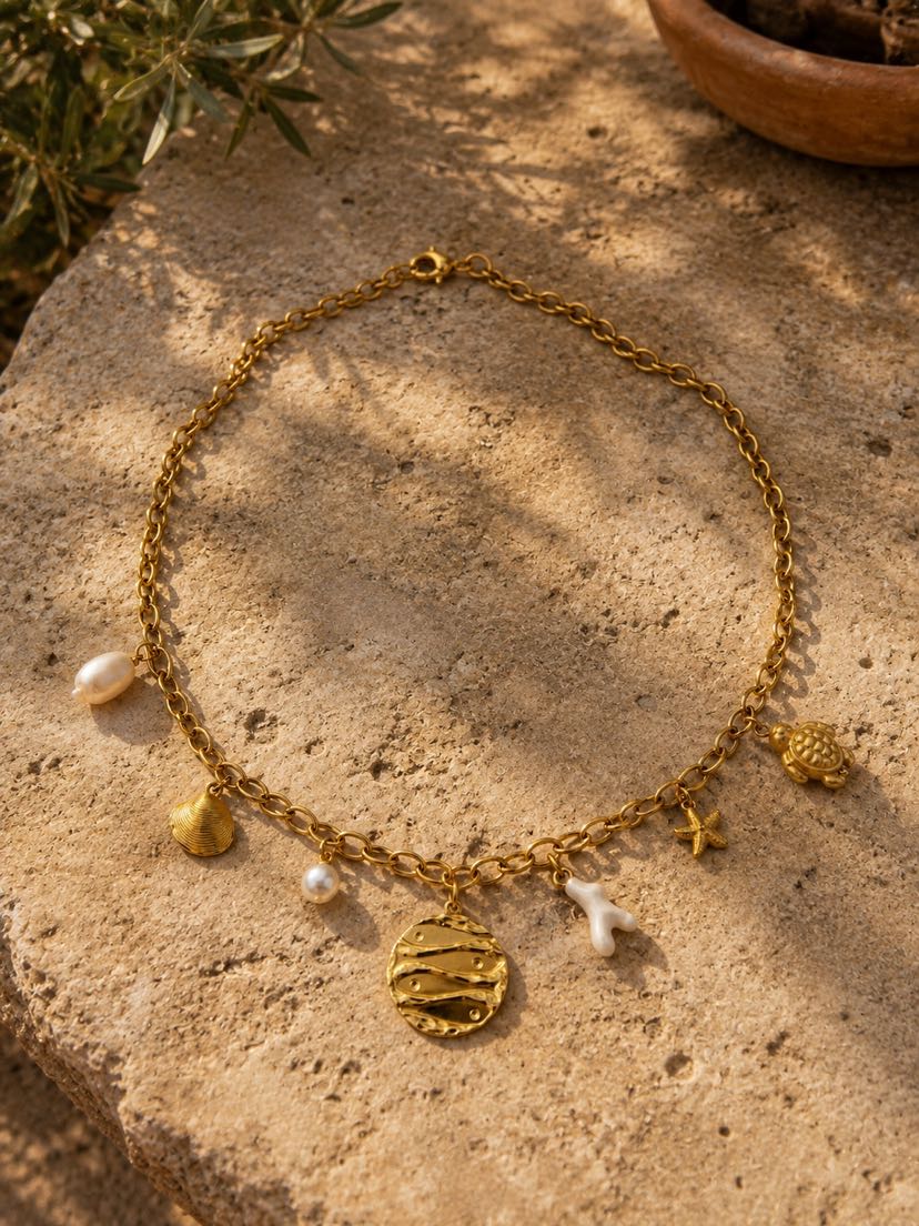 Collier Onda posé sur un bloc de pierre calcaire crème, étiré en arc, ombre dansante de feuilles d'olivier au-dessus, coupe en céramique brune en arrière-plan